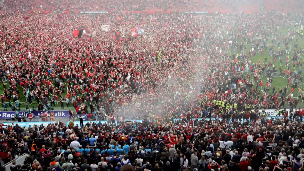 Jubilant Leverkusen fans celebrate on the pitch after the final whistle.